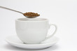 Spoon of instant coffee granules above white cup and saucer