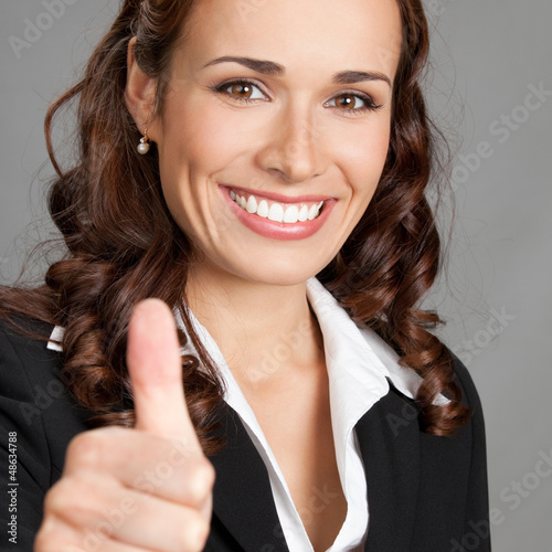 Photo: Businesswoman with thumbs up, over grey Businesswoman with thumbs up, over grey