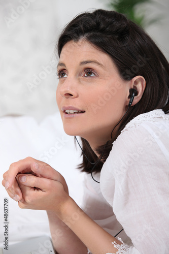 Photo: Woman listening to headphones in bed Woman listening to headphones in bed