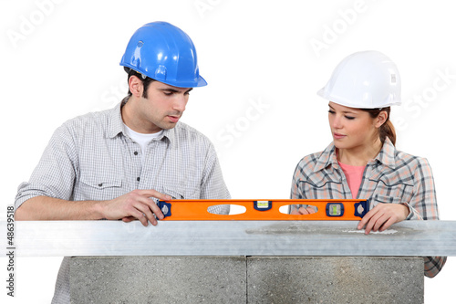 Photo: Couple using spirit-level on wall Couple using spirit-level on wall