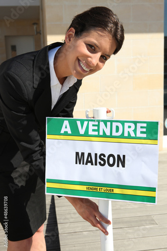 Photo: Woman putting home for sale sign Woman putting home for sale sign