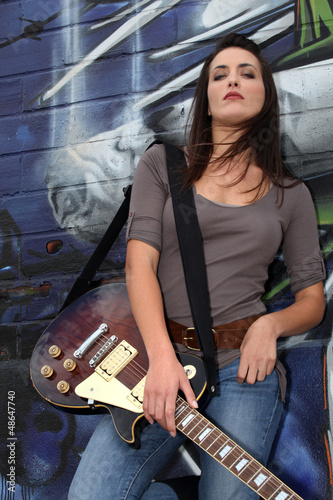 Photo: Cool female guitarist standing against graffiti Cool female guitarist standing against graffiti