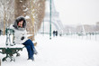 Photo: Beautiful girl in fur hood sitting on a bench near the Eiffel to Beautiful girl in fur hood sitting on a bench near the Eiffel to
