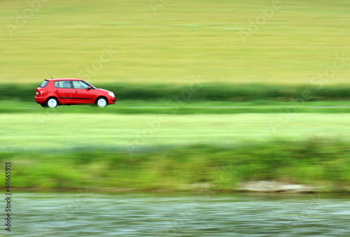 Photo: Panning shot of a fast moving red small car Panning shot of a fast moving red small car