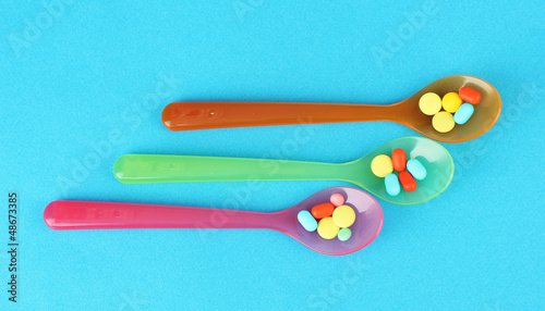 Photo: Plastic spoons with color pills on blue background Plastic spoons with color pills on blue background
