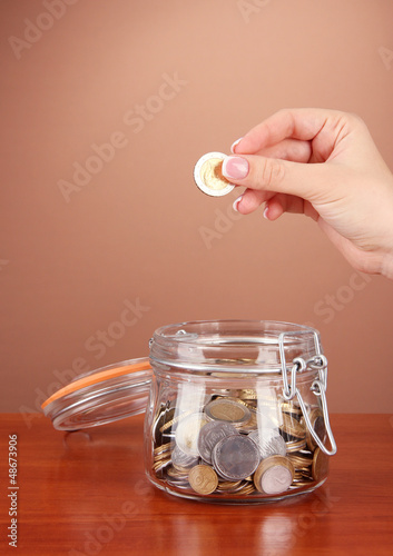 Photo: Saving, female hand putting a coin into glass bottle, Saving, female hand putting a coin into glass bottle,