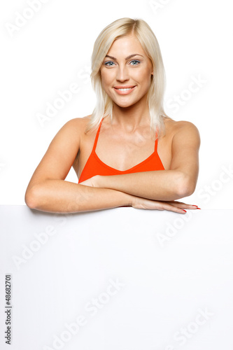 Photo: Smiling woman standing behind and leaning on white billboard Smiling woman standing behind and leaning on white billboard