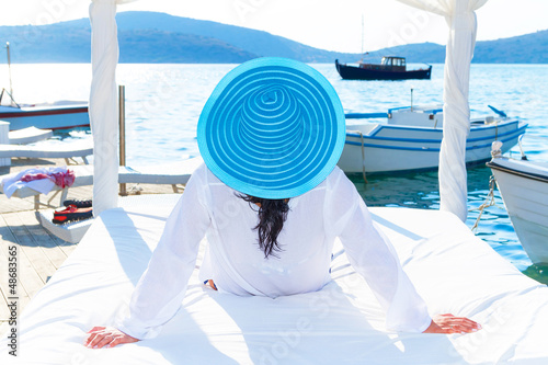 Photo: Woman in hat relaxing on luxury white bed at the sea Woman in hat relaxing on luxury white bed at the sea