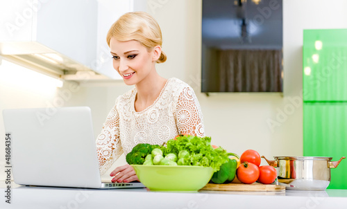 Photo: Woman looking for a recipe on the computer in the kitchen Woman looking for a recipe on the computer in the kitchen