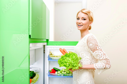 Photo: Smiling young woman taking vegetables out of fridge Smiling young woman taking vegetables out of fridge
