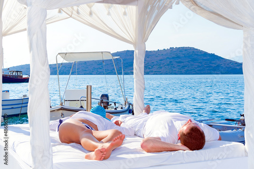 Photo: Couple lying on luxury white bed at the sea Couple lying on luxury white bed at the sea