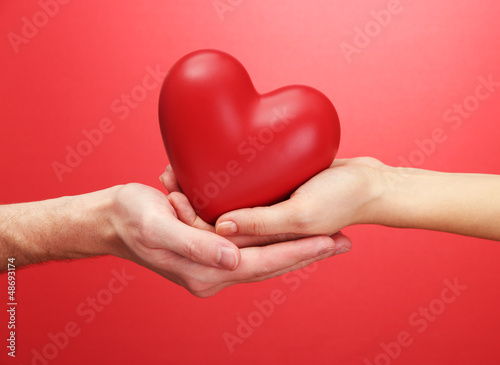 Photo: Red heart in woman and man hands, on red background Red heart in woman and man hands, on red background