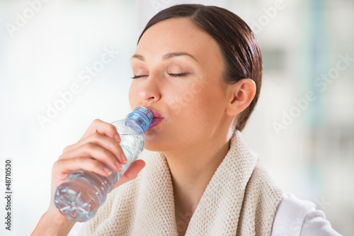 Photo: Portrait of young woman drinking water at gym after doing exerci Portrait of young woman drinking water at gym after doing exerci