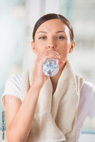 Photo: Portrait of young woman drinking water at gym after doing exerci Portrait of young woman drinking water at gym after doing exerci