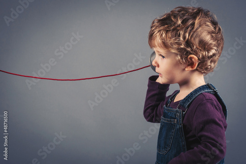 Photo: Young kid listen to tin can telephone. Young kid listen to tin can telephone.