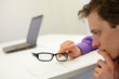 thinking man holding eyeglasses - notebook in background