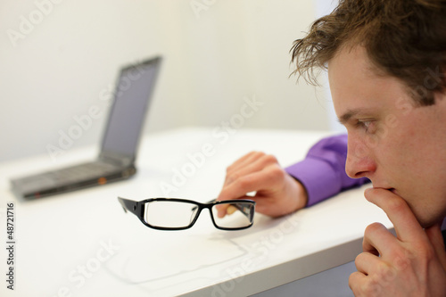 Photo: thinking man holding eyeglasses - notebook in background thinking man holding eyeglasses - notebook in background