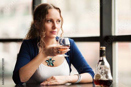 Photo: Beautiful young woman with cognac looking out the window Beautiful young woman with cognac looking out the window