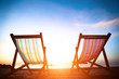 Pair of beach loungers on the deserted coast sea at sunrise.
