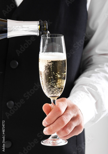 Photo: Portrait of a waiter pouring champagne into a flute Portrait of a waiter pouring champagne into a flute
