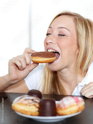 Photo: Pretty woman takes a bite of a donut with closed eyes Pretty woman takes a bite of a donut with closed eyes