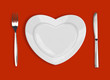 plate in shape of heart, table knife and fork on red background