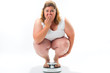 Obese young woman crouching on a scale