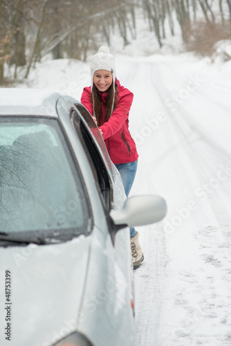 Photo: The girl is pushing a broken car on the road in winter The girl is pushing a broken car on the road in winter