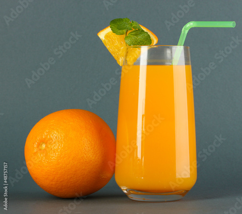 Photo: Glass of orange juice with mint and orange on grey background Glass of orange juice with mint and orange on grey background