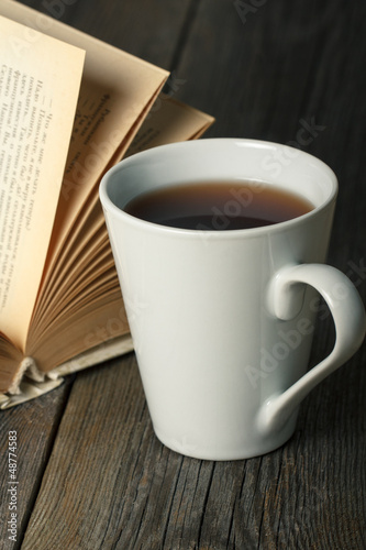 Photo: Cup of tea with old opened book on wooden table. Cup of tea with old opened book on wooden table.