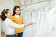 Shop assistant  helps bride in choosing  dress