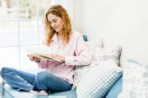 Photo: Woman reading book by window Woman reading book by window