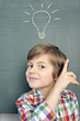 Kind mit Idee-Symbol vor Schultafel