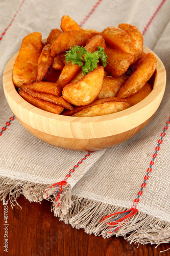 Photo: Appetizing village potatoes in bowl on wooden table close-up Appetizing village potatoes in bowl on wooden table close-up