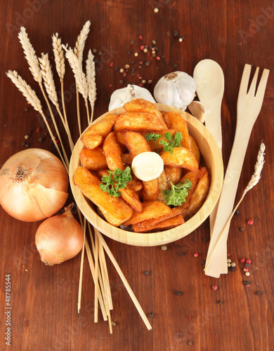 Photo: Appetizing village potatoes in bowl on wooden table close-up Appetizing village potatoes in bowl on wooden table close-up