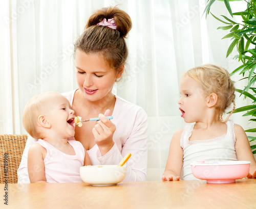 Photo: young mother feeding her two daughters from a spoon young mother feeding her two daughters from a spoon