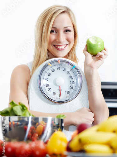 Photo: Girl with scale and fruits in kitchen is proud to lose weight Girl with scale and fruits in kitchen is proud to lose weight