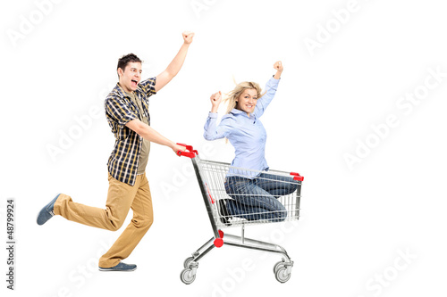 Photo: Full length portrait of a young man pushing a woman in a shoppin Full length portrait of a young man pushing a woman in a shoppin