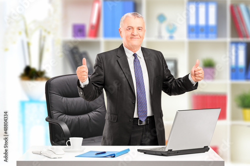 Photo: Businessman posing in his office and giving a thumb up Businessman posing in his office and giving a thumb up