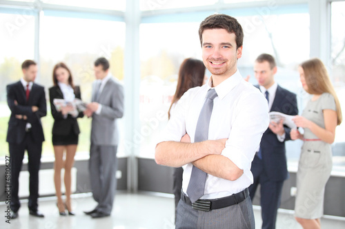 Photo: Handsome happy business man with colleagues at the back Handsome happy business man with colleagues at the back