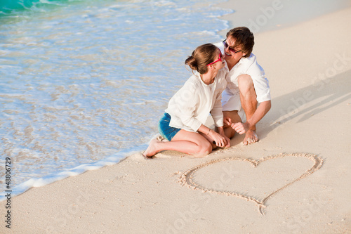 Photo: portrait of young happy couple drawing a heart on the sand portrait of young happy couple drawing a heart on the sand