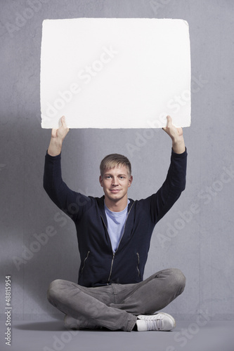 Photo: Joyous man holding up white blank panel. Joyous man holding up white blank panel.
