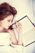Pretty red-haired woman sleeping in the bed near book. Studio sh