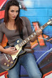 Female guitarist stood by painted wall