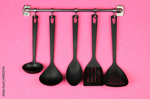 Photo: Black kitchen utensils on silver hooks, on pink background Black kitchen utensils on silver hooks, on pink background