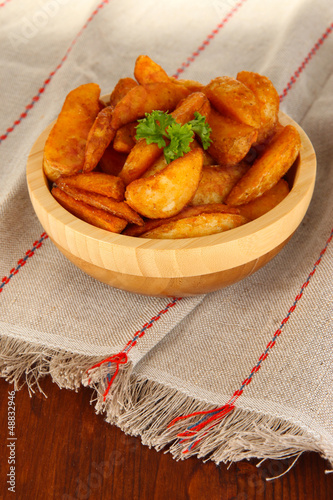 Photo: Appetizing village potatoes in bowl on wooden table close-up Appetizing village potatoes in bowl on wooden table close-up