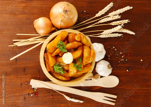 Photo: Appetizing village potatoes in bowl on wooden table close-up Appetizing village potatoes in bowl on wooden table close-up