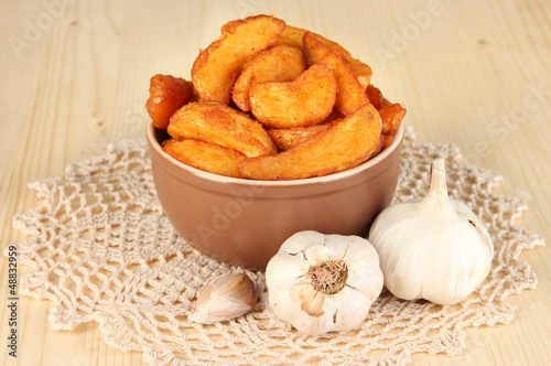 Photo: Appetizing village potatoes in bowl on wooden table close-up Appetizing village potatoes in bowl on wooden table close-up