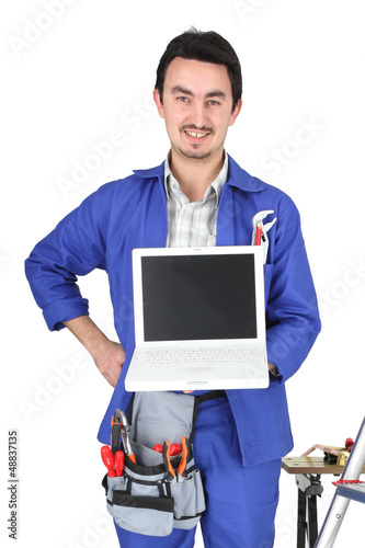 Photo: 30 years old artisan showing a laptop in a room full of tools 30 years old artisan showing a laptop in a room full of tools