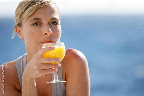 Photo: Woman enjoying glass of orange juice by the sea Woman enjoying glass of orange juice by the sea